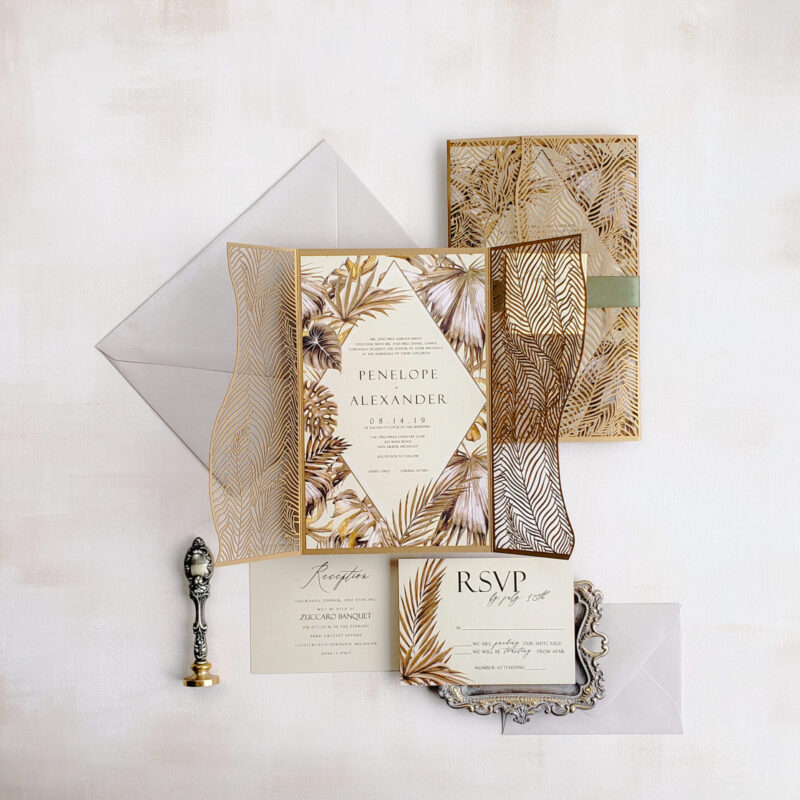 Luxury tropical laser cut wedding invitations featuring an intricate gold gate fold design with a tropical motif, perfect for destination weddings.