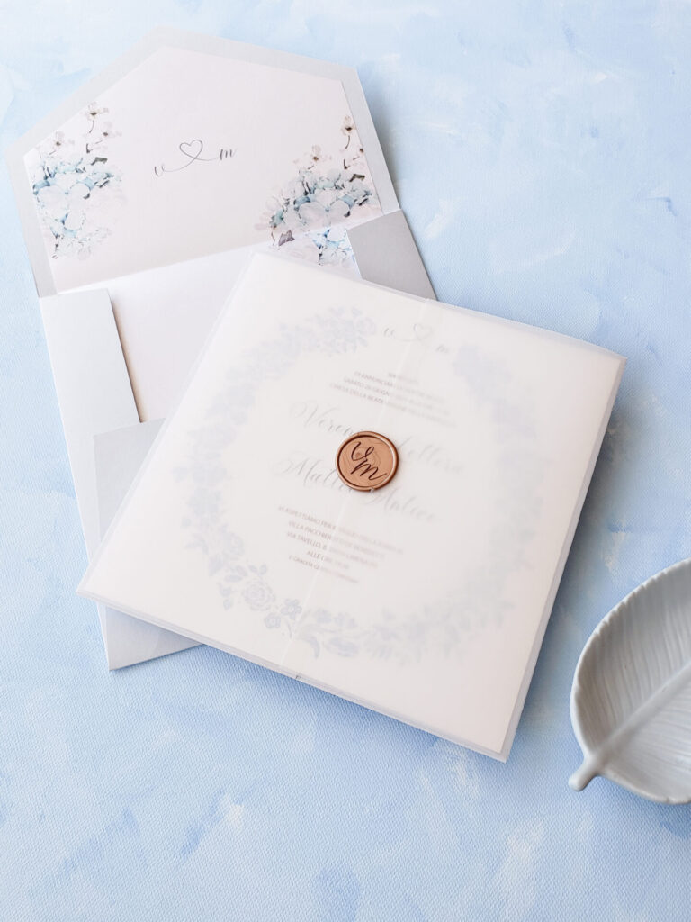 Soft blue and hydrangea-inspired wedding invitation suite with a floral envelope liner, vellum wrap, and wax seal closure.