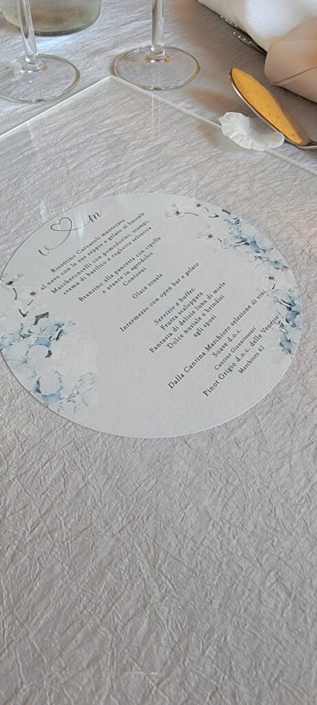 Round wedding menu with soft blue hydrangea illustrations, printed on textured cardstock, placed on an elegant reception table setting.